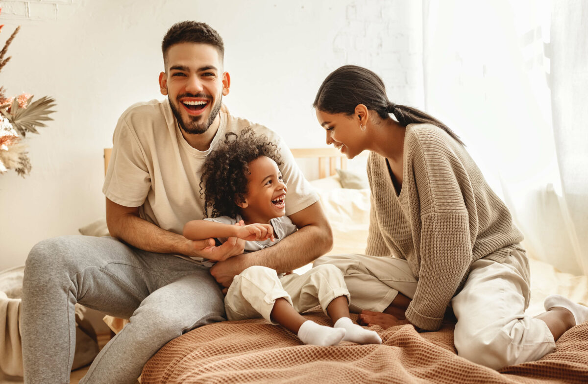 Vater, Mutter und Kind lachend im Schlafzimmer