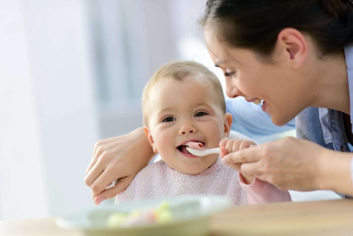 Baby lernt Essen mit Löffel, Mutter lächelt