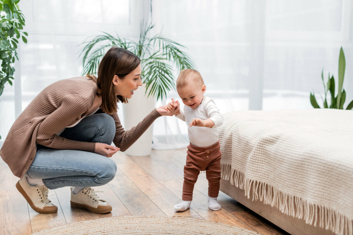 Baby übt Laufen mit seiner Mutter, beide lächeln